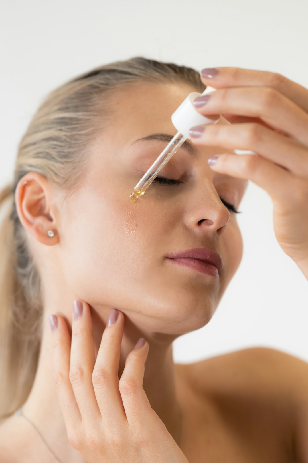 A woman applying a drop of facial serum from a glass dropper